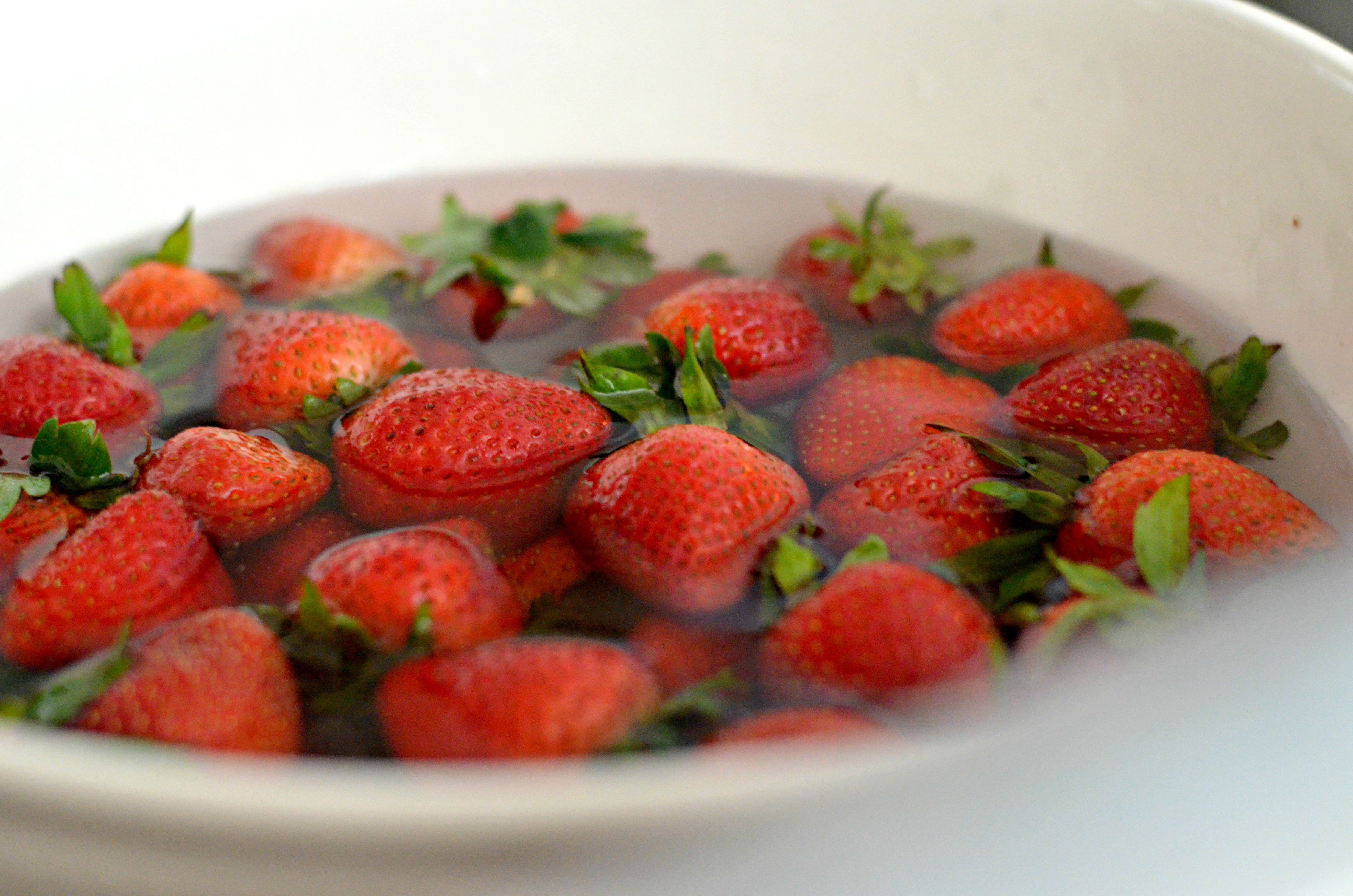 tons of red fresh strawberries soaking in bowl of vinegar