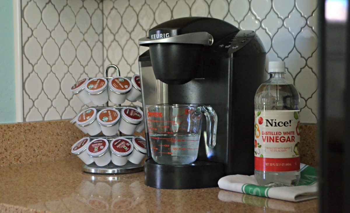 A measuring cup sitting on Keurig coffee maker as a use for vinegar to descale coffee makers