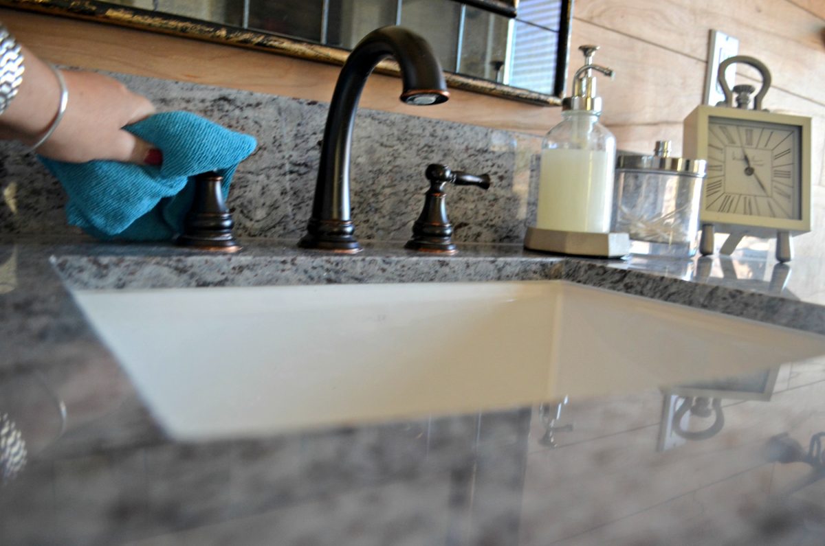 hand holding a blue towel wiping down bathroom faucet handles