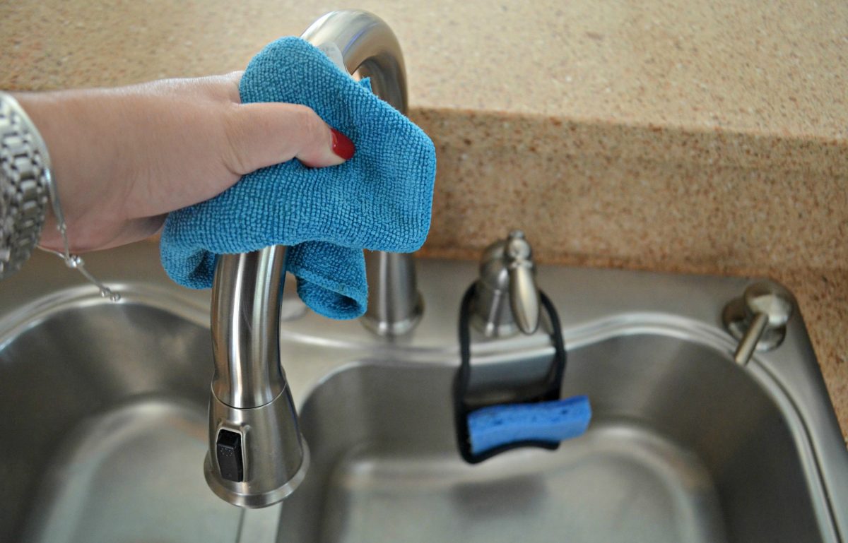 hand holding a blue towel shining a stainless steel faucet handle