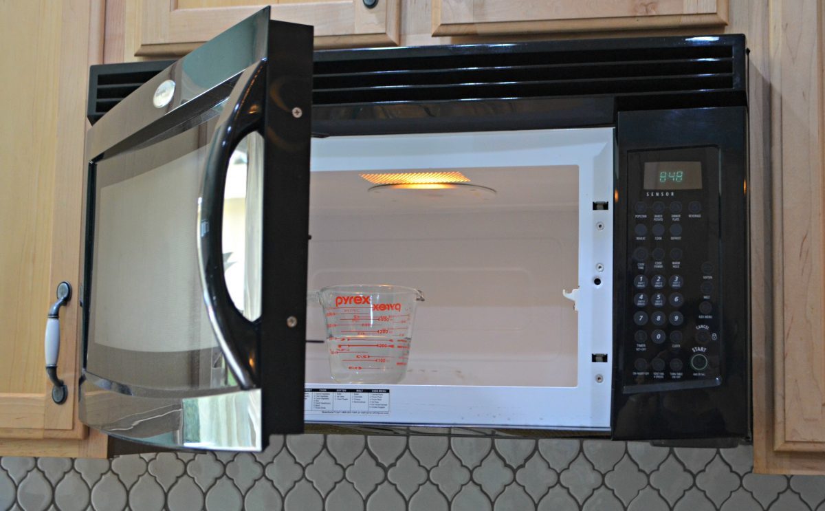 a measuring glass with vinegar in a microwave with door open