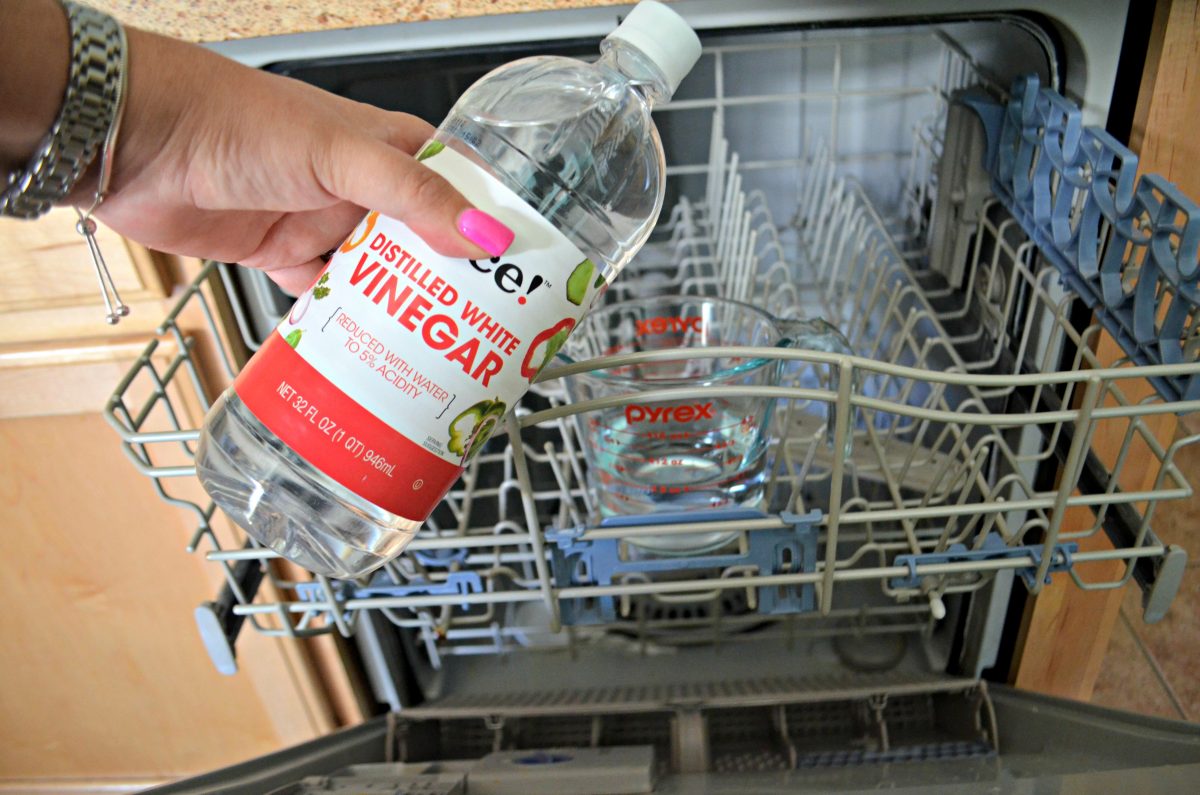 hand holding a bottle of vinegar over open dishwasher