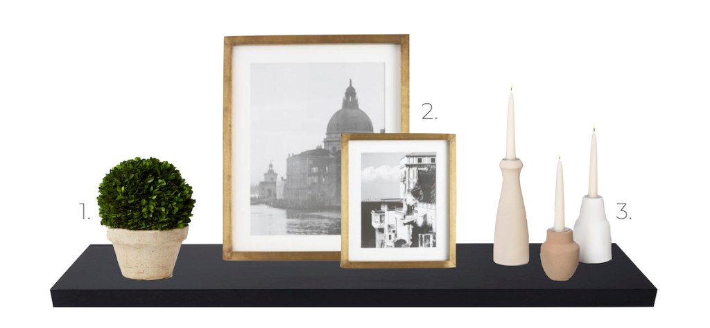 black shelf with faux boxwood plant gold matte frame and three beige tan candle holders 