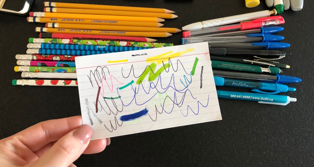 various colors of scribbles on paper with pens and pencils in the background