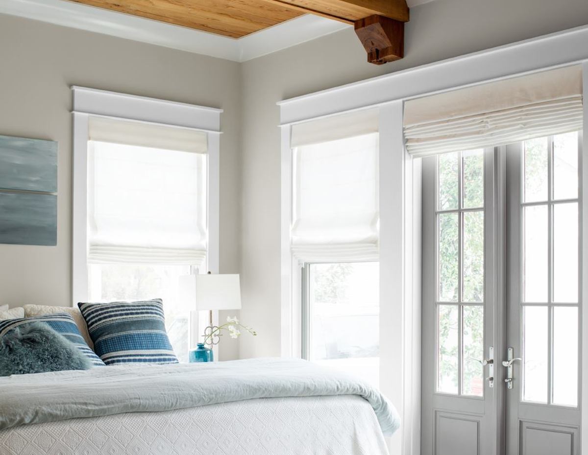 neutral color walls with windows wood ceiling and bed with blue stripe pillows gray french doors
