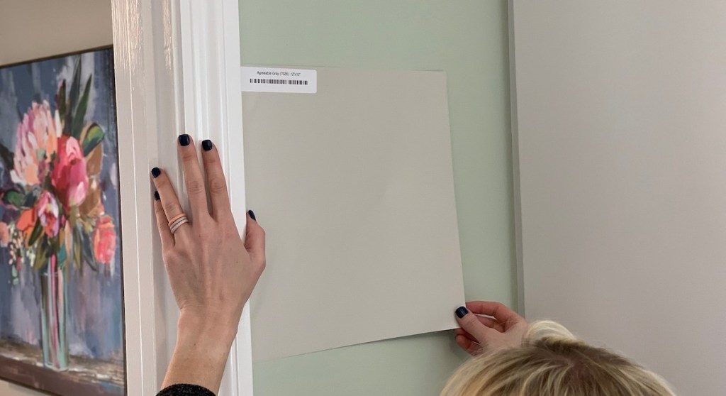 hands placing gray paint sample on wall floral artwork in background
