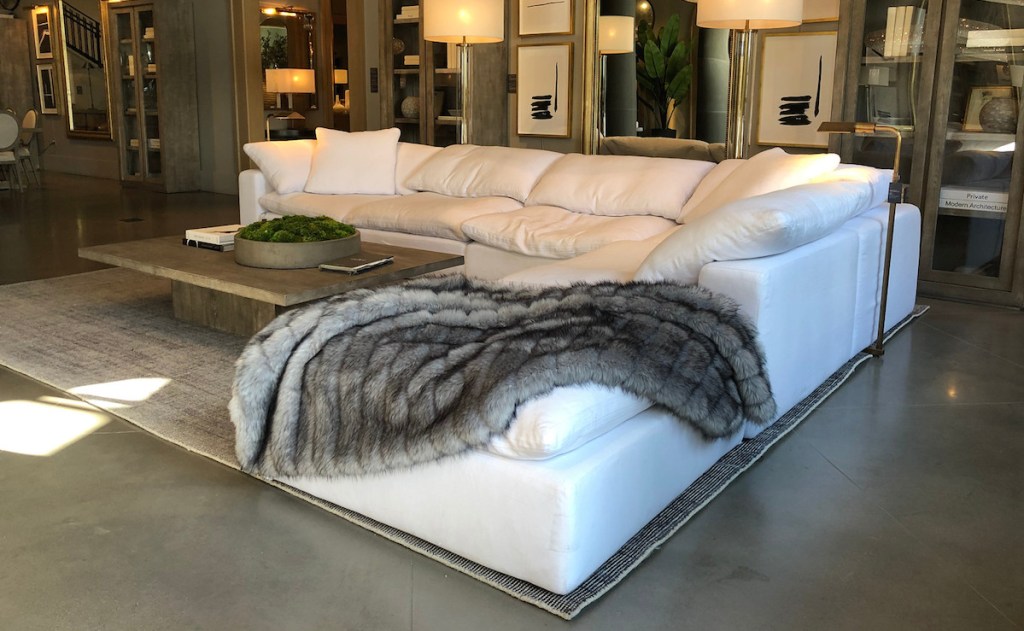 a white sectional couch with gray fur blanket on top with rug and coffee table 
