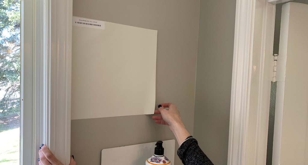 hand peeling off corner of white square paint sample from gray wall