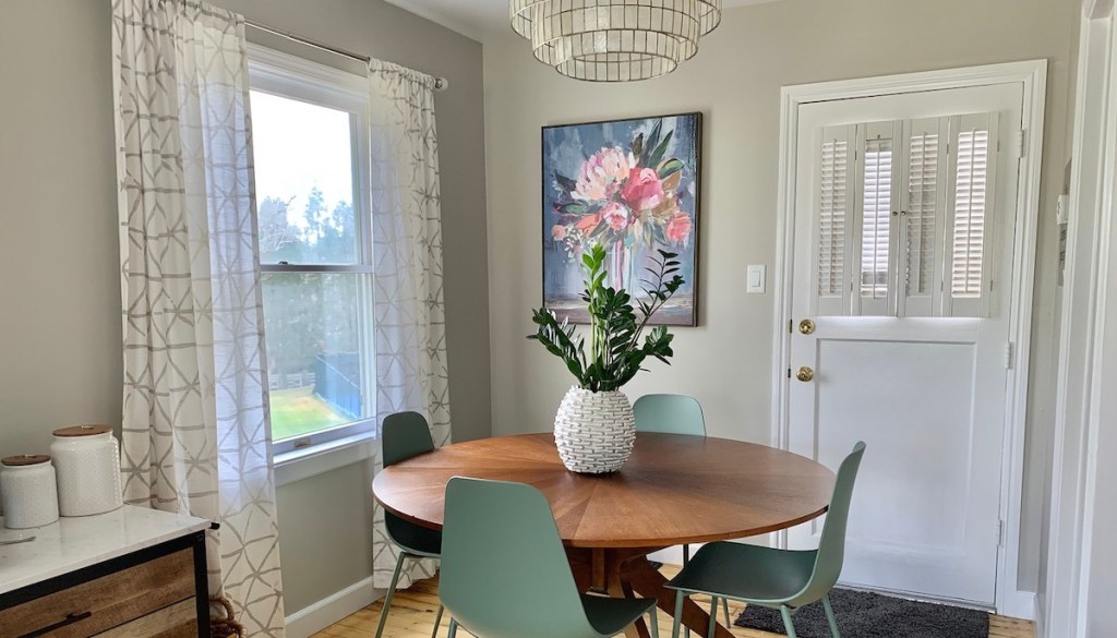 breakfast nook with flower artwork white curtains round wood table with blue green chairs