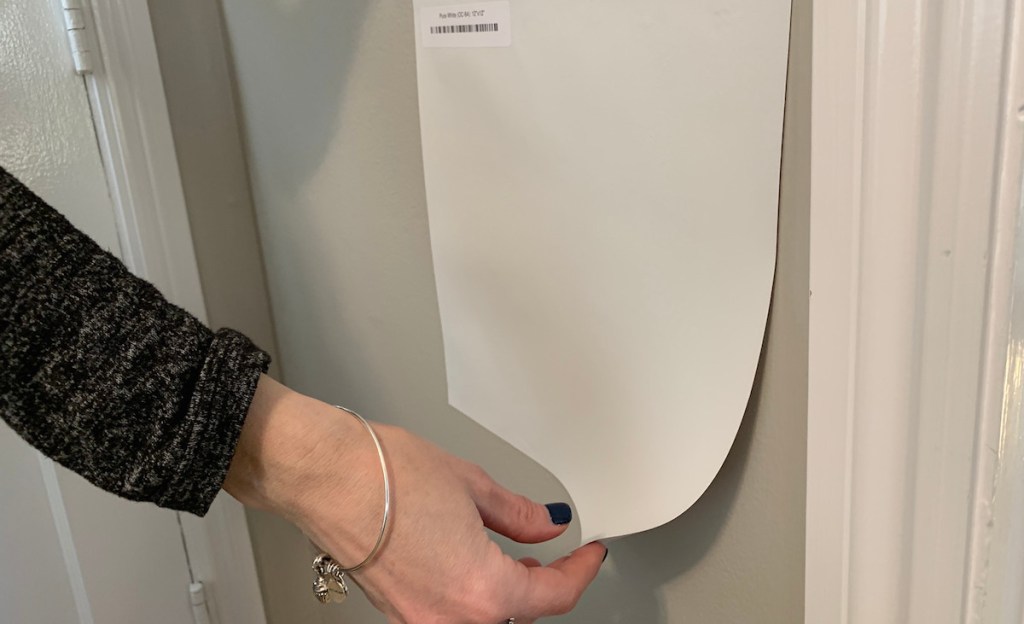 collins hand peeling off a white square paint sample on a gray wall