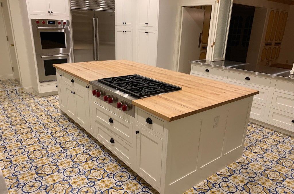 large butcher block island with stainless steel range red knobs white cabinets and mexican style tile floor