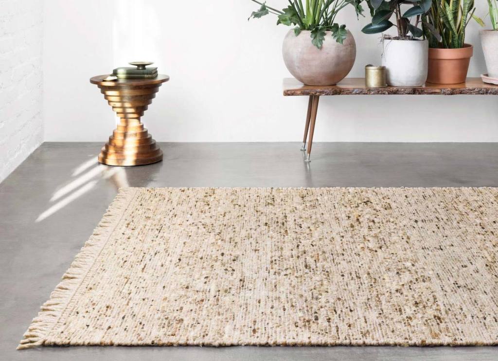 natural colored rug on concrete floor with planters and greenery on bench in background