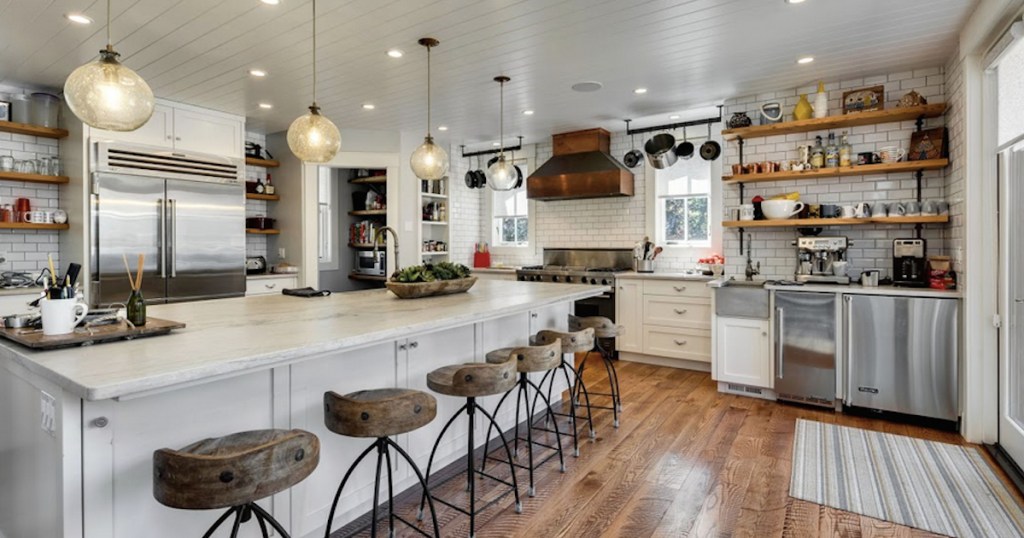 huge white kitchen with copper range hood and wood and iron barstools lined up at island counter
