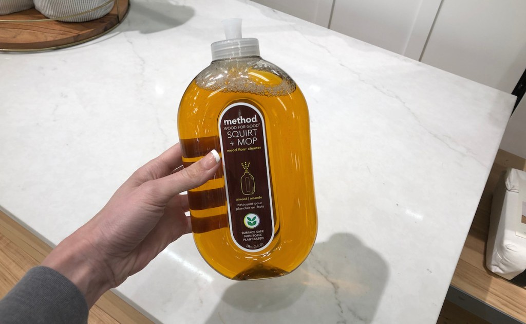 hand holding method wood floor cleaner over marble countertop