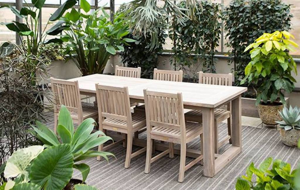 light wood patio table and chairs surrounded by green plants