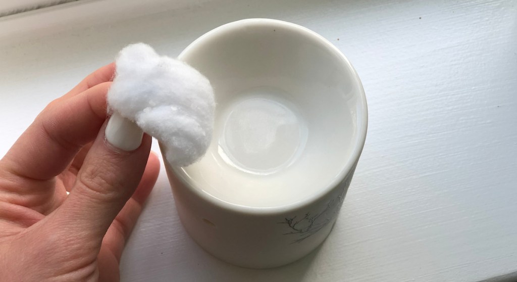 hand holding a white cotton ball with glass wax melt sitting on window sill