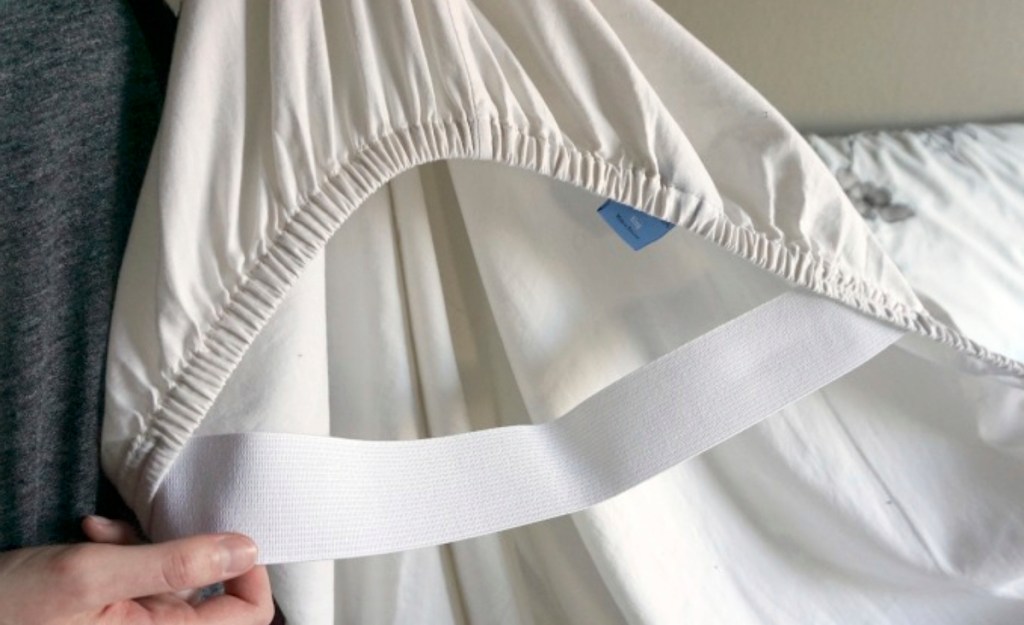 hand holding white fitted sheet with white elastic on corner