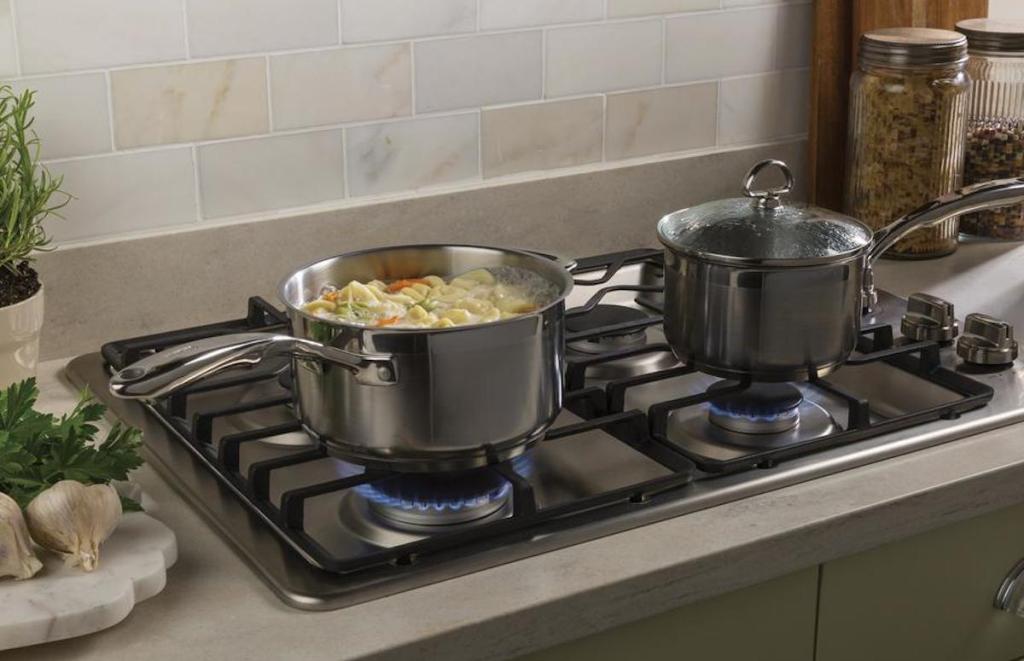 gas range with two stainless steel pots with noodle soup boiling with tile backsplash