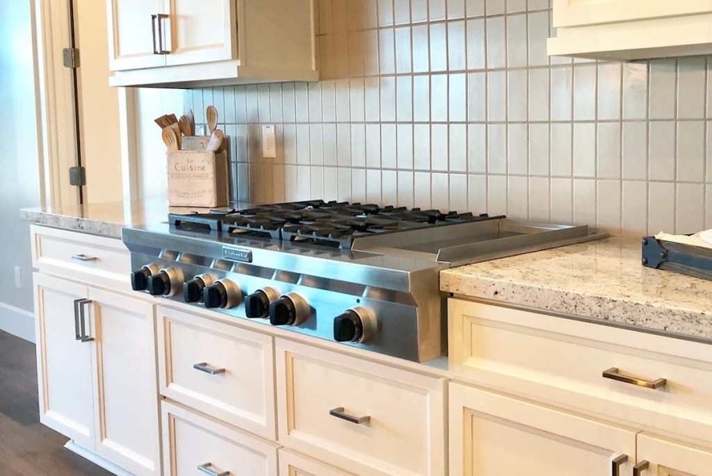 stainless steel kitchaid gas cooktop with black knobs on granite counter with cream shaker cabinets