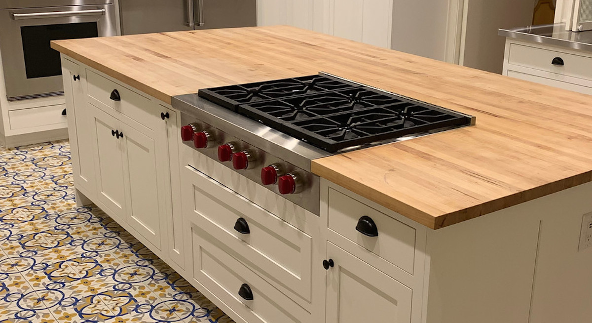 wolf gas stainless steel cooktop with red knobs on butcher block countertop white cabinets