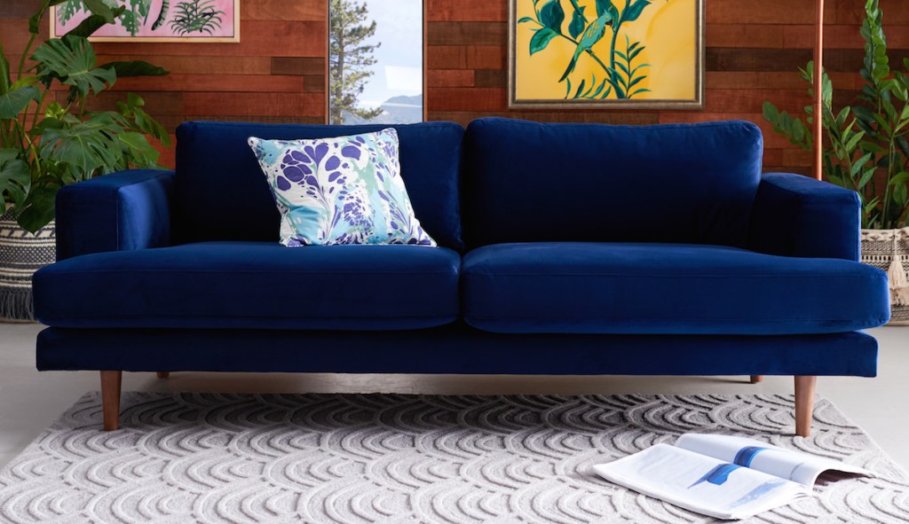 navy velvet couch in room with ivory textile rug and various bold decor pillows