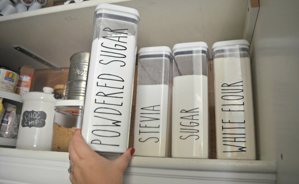 hand pulling clear container of powdered sugar off pantry shelf
