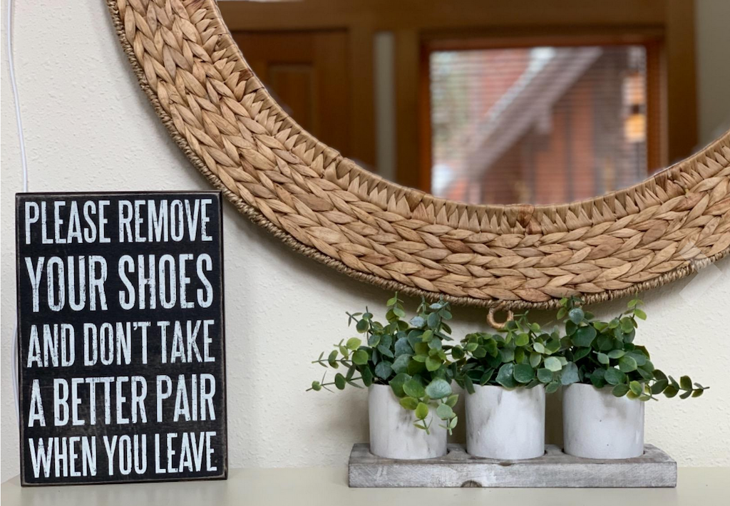 remove your shoes sign sitting on table with plants and mirror