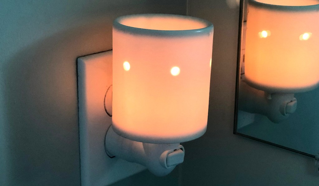 white wax melt plugged into wall with light on and reflection in the mirror