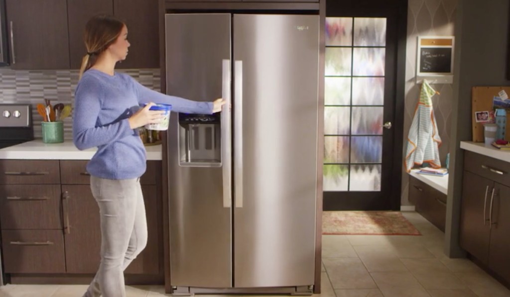 woman opening side by side stainless steel refrigerator door with brown wood cabinets surrounding it