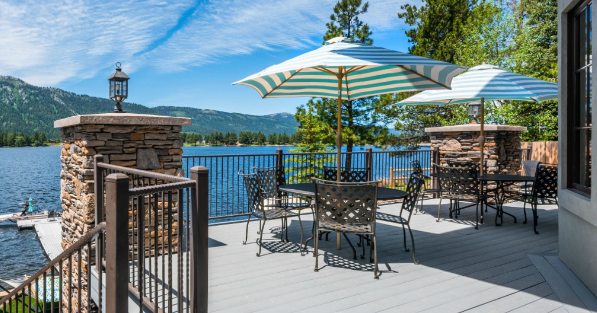 blue and white striped umbrella with table on deck with water and trees in the background