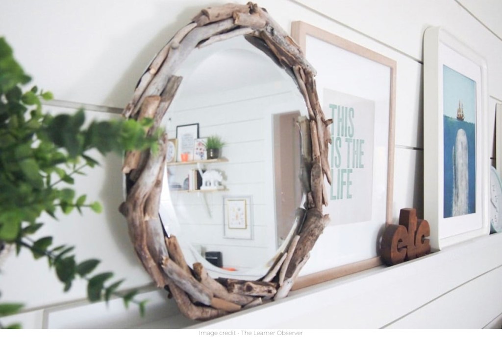 round driftwood mirror sitting on white shelf with artwork