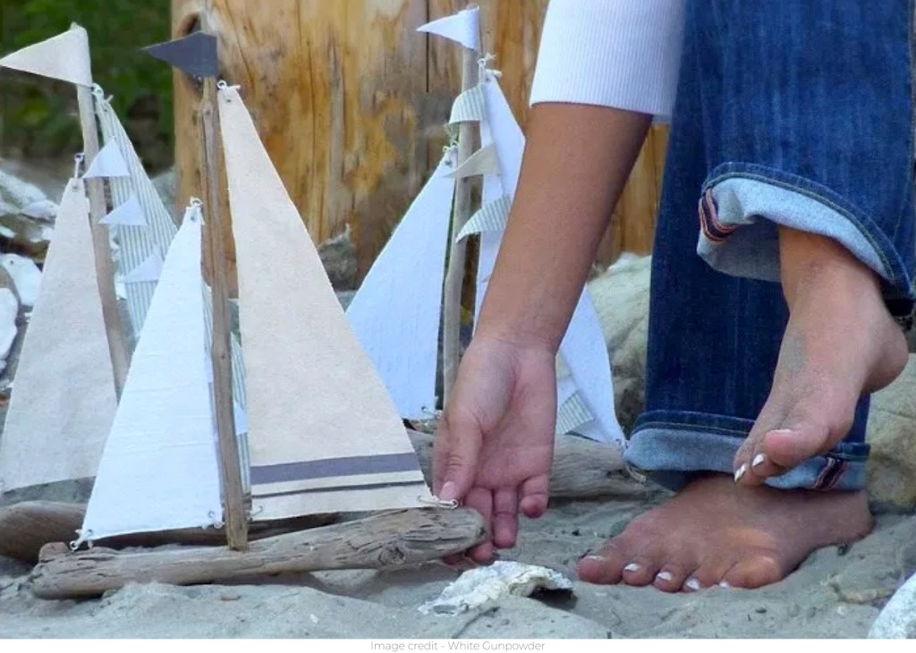 person holding driftwood sailboats on sandy beach