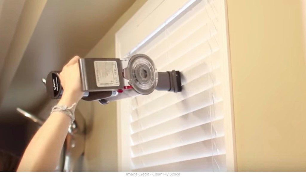 person vacuuming white blinds