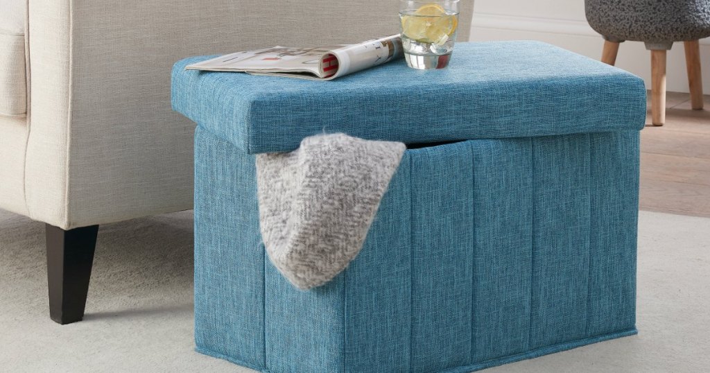 blue storage ottoman with blanket inside next to chair 