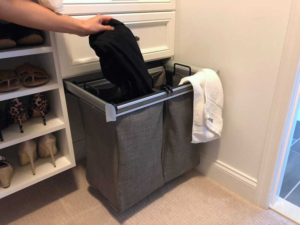 hand holding black clothing over laundry sorter