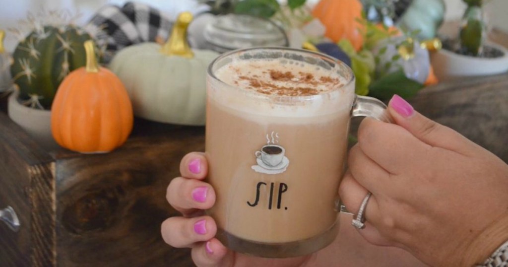 living Hygge lifestyle while holding latte with pumpkins and fall decor in the background 