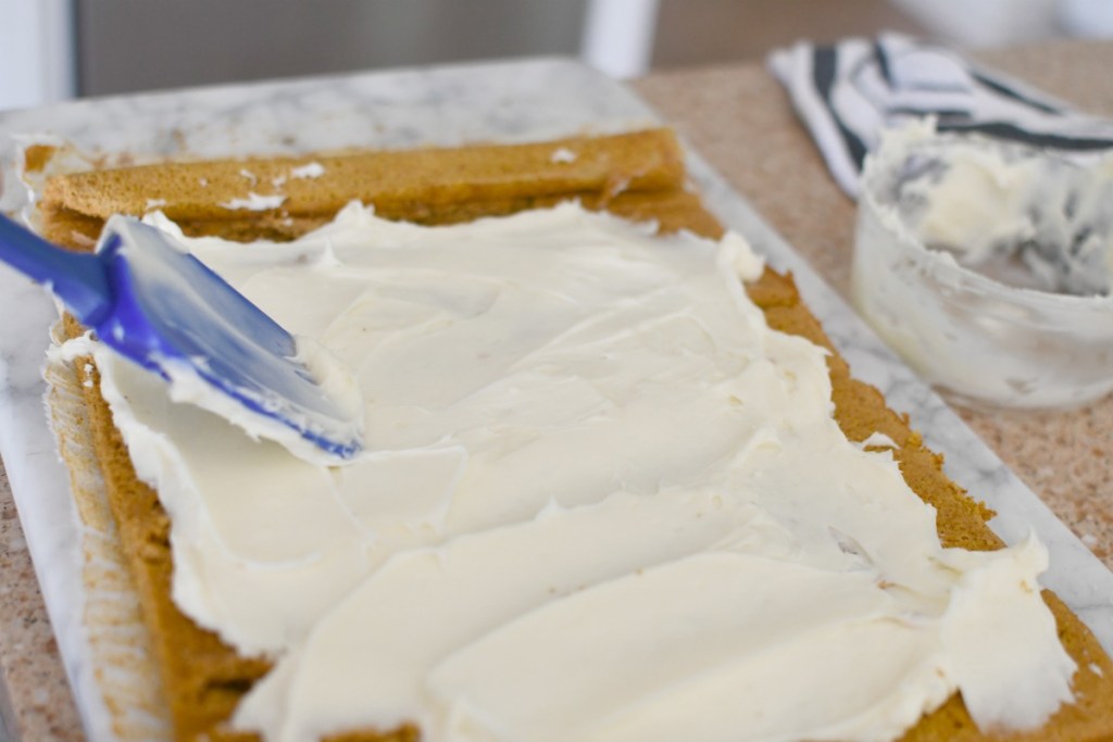 spreading frosting on a pumpkin roll