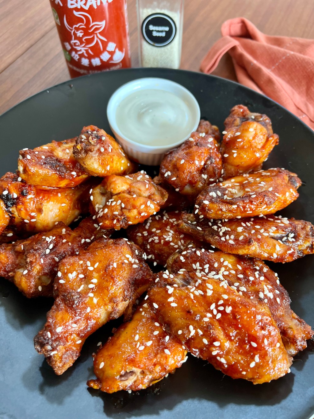 large plate of sriratcha honey baked wings with sesame seeds on a black plate