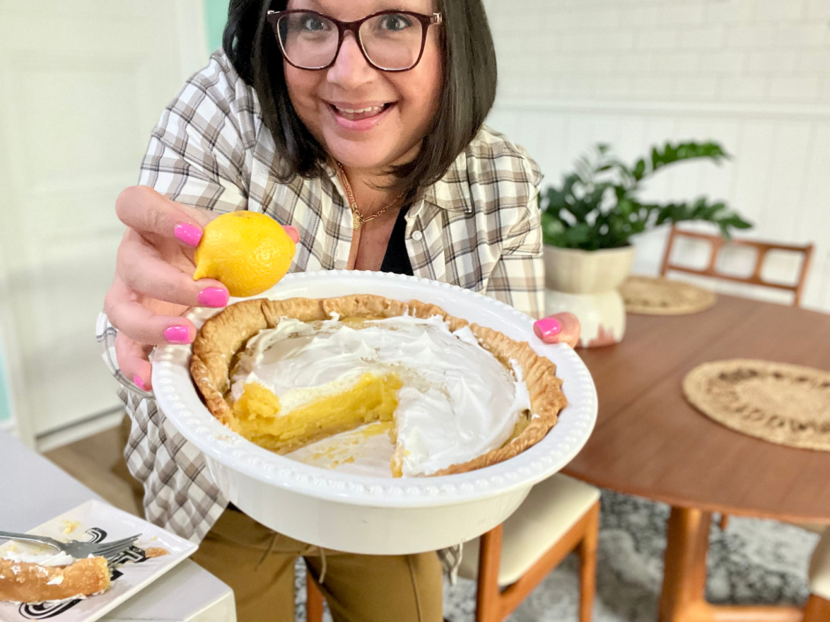 A woman is holding a finished pie while also holding a lemon.