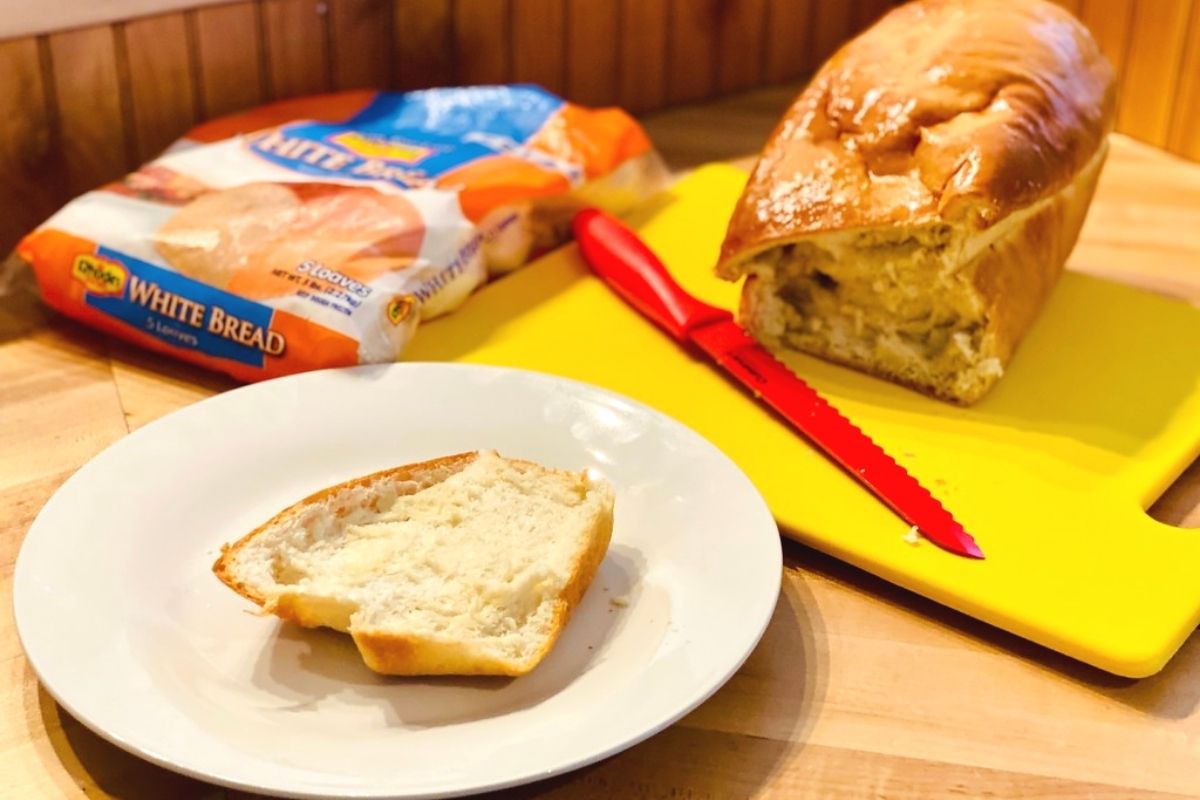 A slice of fresh bread on a plate next to the loaf