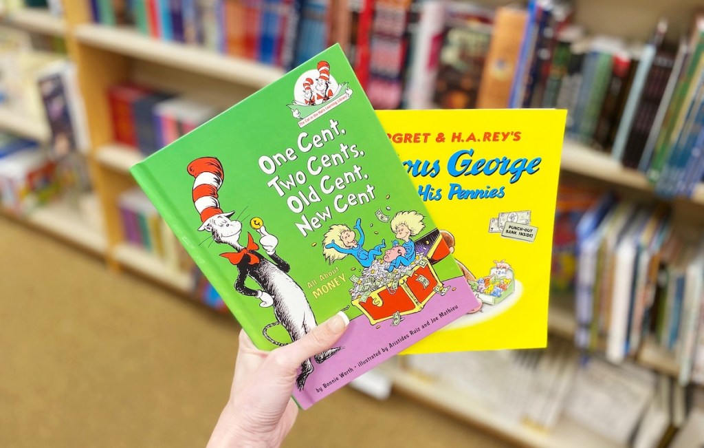 hand holding green and yellow kids books with bookshelves in background