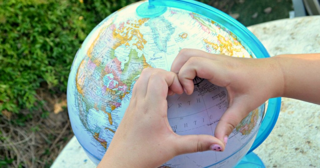 person making heart shape with hands over globe