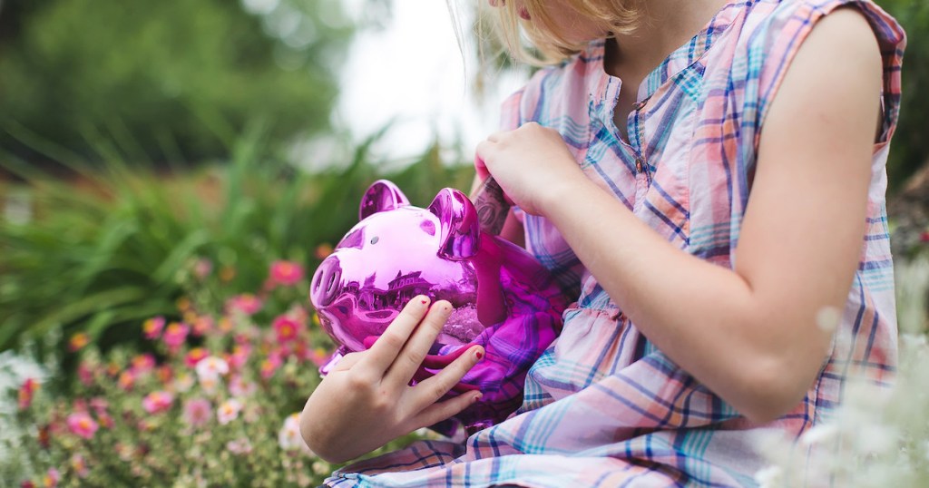 girl holding purple and pink shiny piggy bank outside