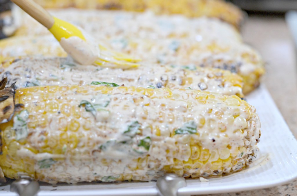 spreading mexican street corn with mayo and sour cream