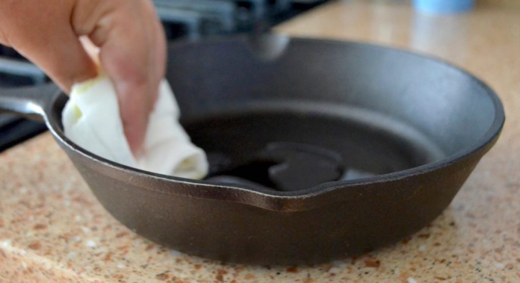 hand holding a white paper towel rubbing oil on black cast iron pan