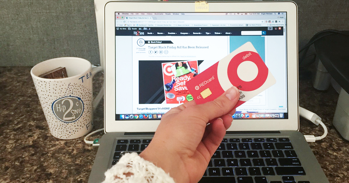 Hand holding Target redcard in front of a computer screen with a Hip2Save mug