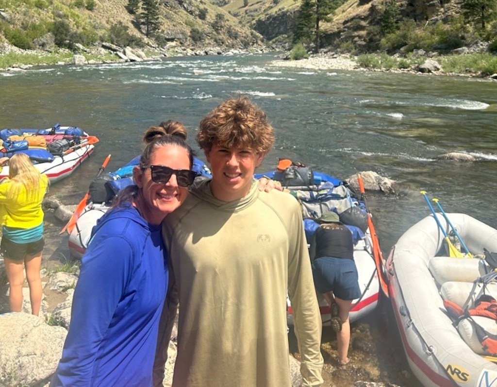 woman and teen boy standing in front of water rafts