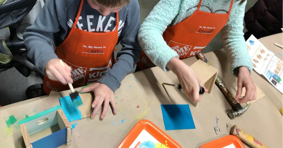 kids wearing orange the home depot aprons with woodworking crafts on table