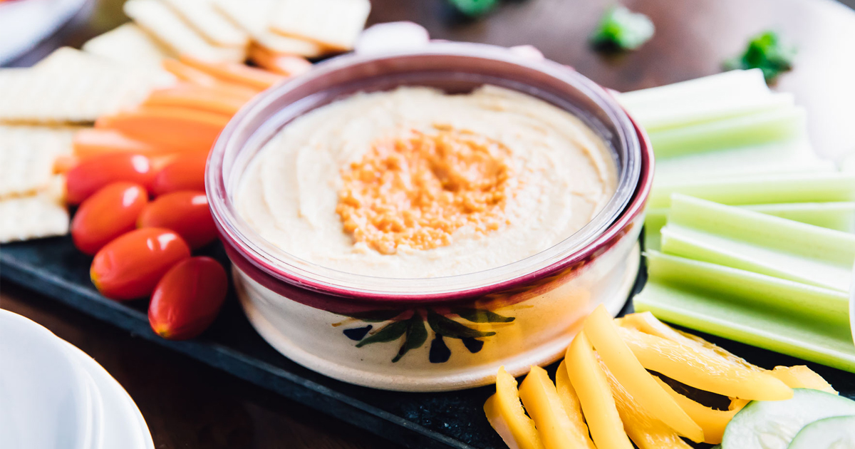 a container of hummus on a tray with vegetables