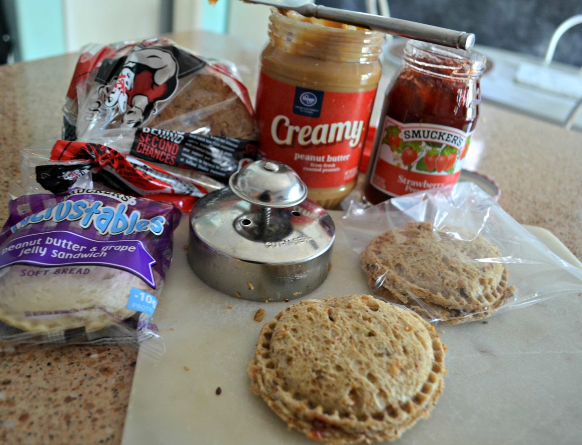 Press and seal PB&J uncrustable maker and sandwich with peanut butter and jelly in background